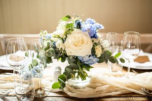 Elegant wedding table centerpiece featuring white roses, blue hydrangeas, and eucalyptus greenery.