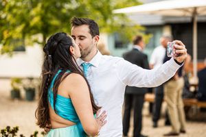 Couple sharing a kiss while taking a selfie at outdoor wedding celebration.