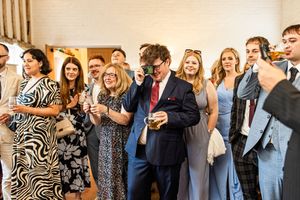Wedding guests laughing and celebrating during a reception toast in a bright venue.