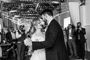 Bride and groom sharing their first dance in black and white with fairy lights above.