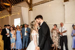 Bride and groom kissing during first dance under fairy lights at wedding reception.