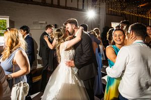 Bride and groom kissing on the dance floor surrounded by celebrating wedding guests.