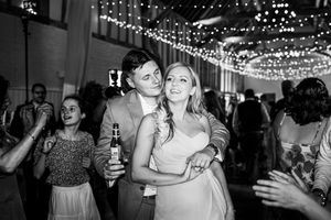 Couple dancing together in black and white photo under fairy lights at reception.