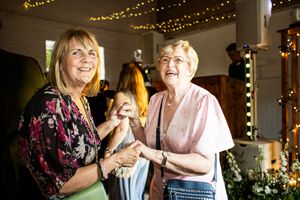 Two older women smiling and holding hands on the wedding dance floor.