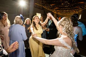 Bride dancing joyfully with guests in yellow dress under fairy lights at reception.