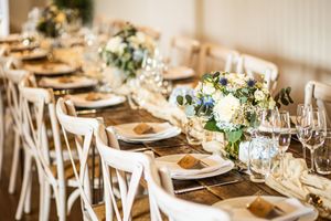 Close-up of a rustic wedding reception table with blue and white floral arrangements, gold charger plates, and crystal glassware.
