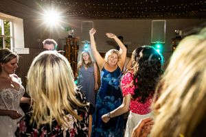 Guests dancing joyfully at a wedding reception with colorful lights and raised hands.