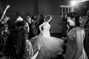 Bride in white gown dancing with guests at wedding reception in black and white photo.