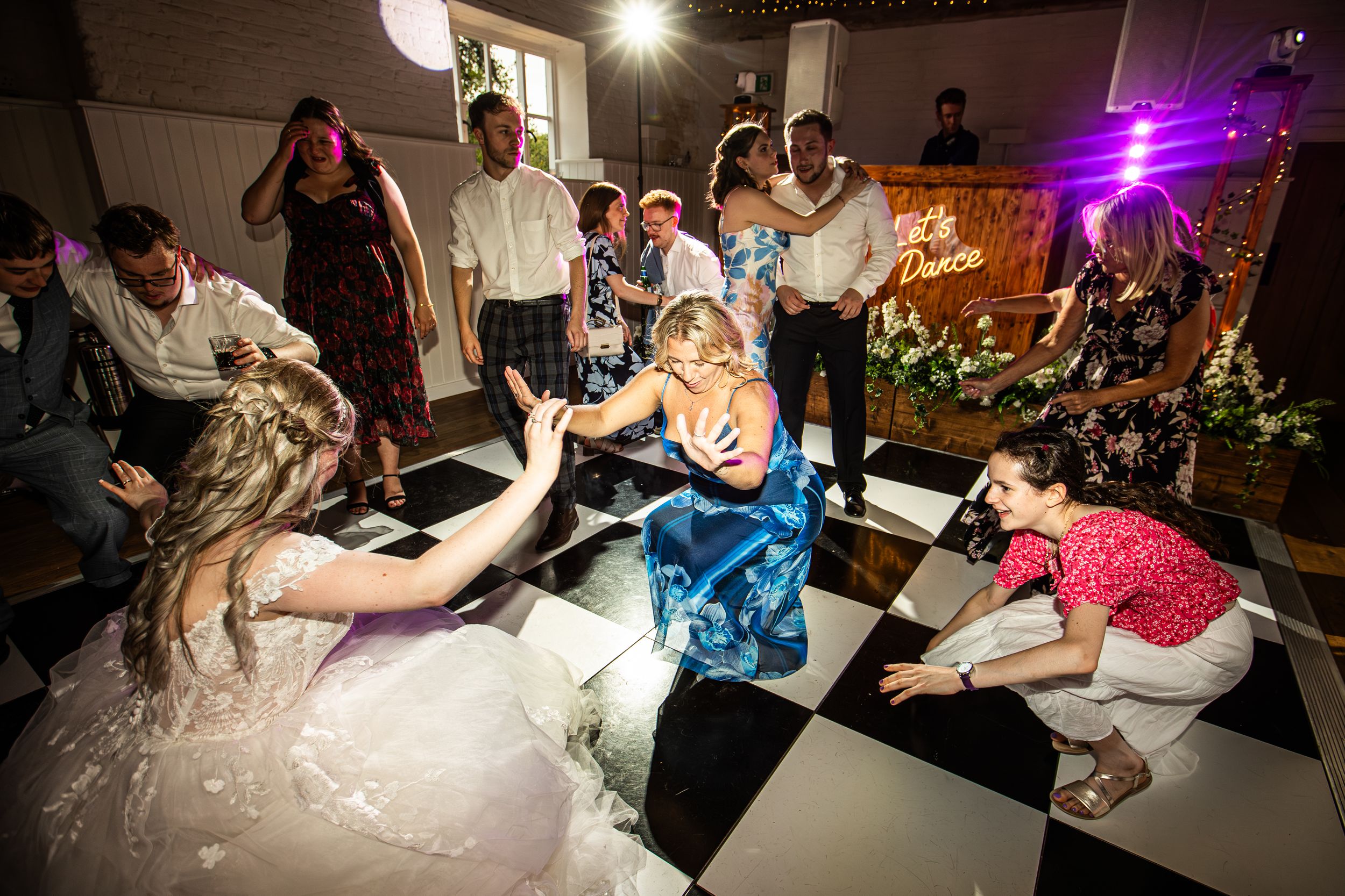 Bride and guests dancing energetically on black and white checkered dance floor at wedding.