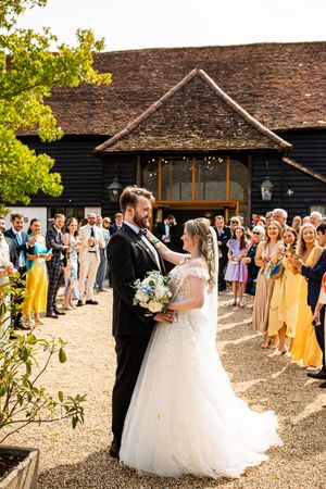 Newlyweds sharing a romantic moment during a confetti exit outside a black timber barn wedding venue with guests cheering.