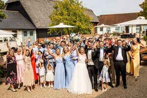 Large wedding group photo with bride, groom, and guests celebrating outdoors in front of a rustic barn venue.