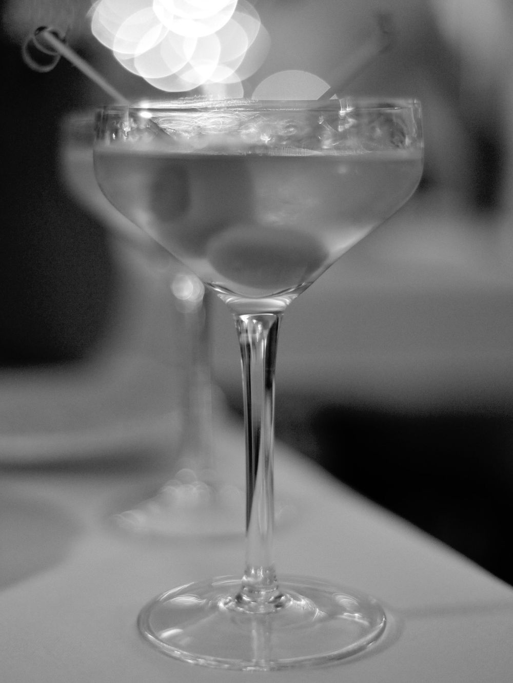 A row of elegant cocktail glasses filled with clear martinis lined up on a bar counter in black and white.