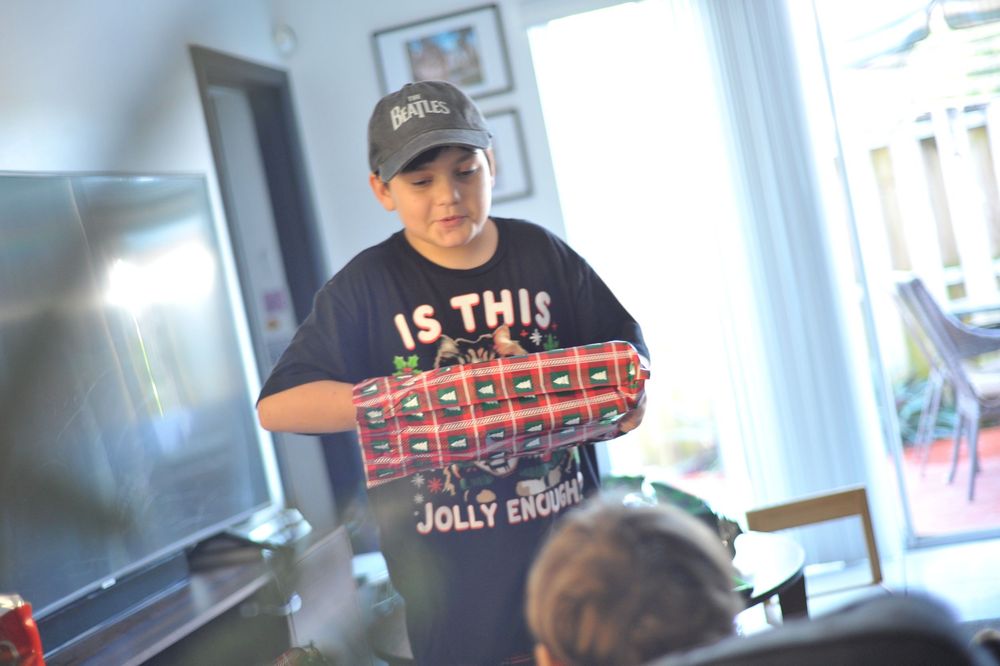 A person in a baseball cap stacks multiple red boxes while working in a retail or warehouse setting.