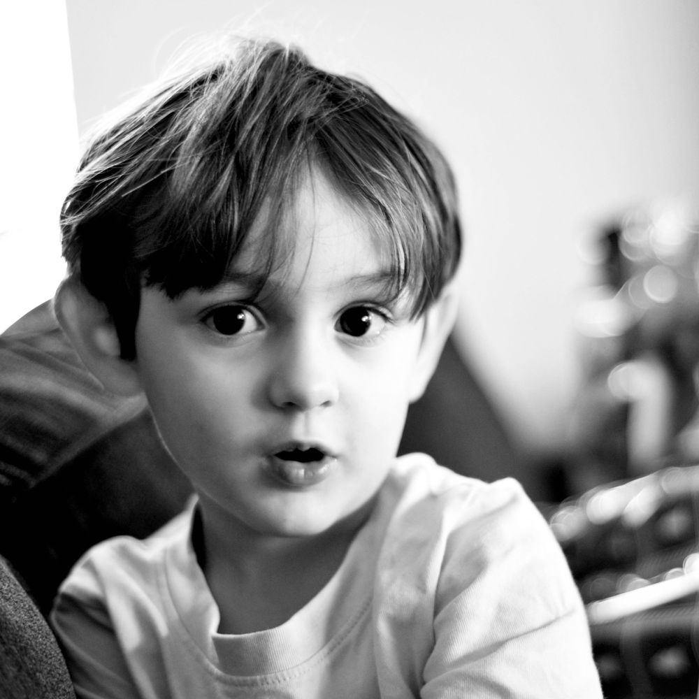 A close-up black and white portrait of a child in a white t-shirt against a light background.