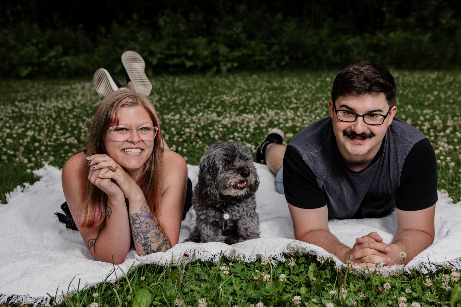 Family and pets lying on white blanket in green grass field.