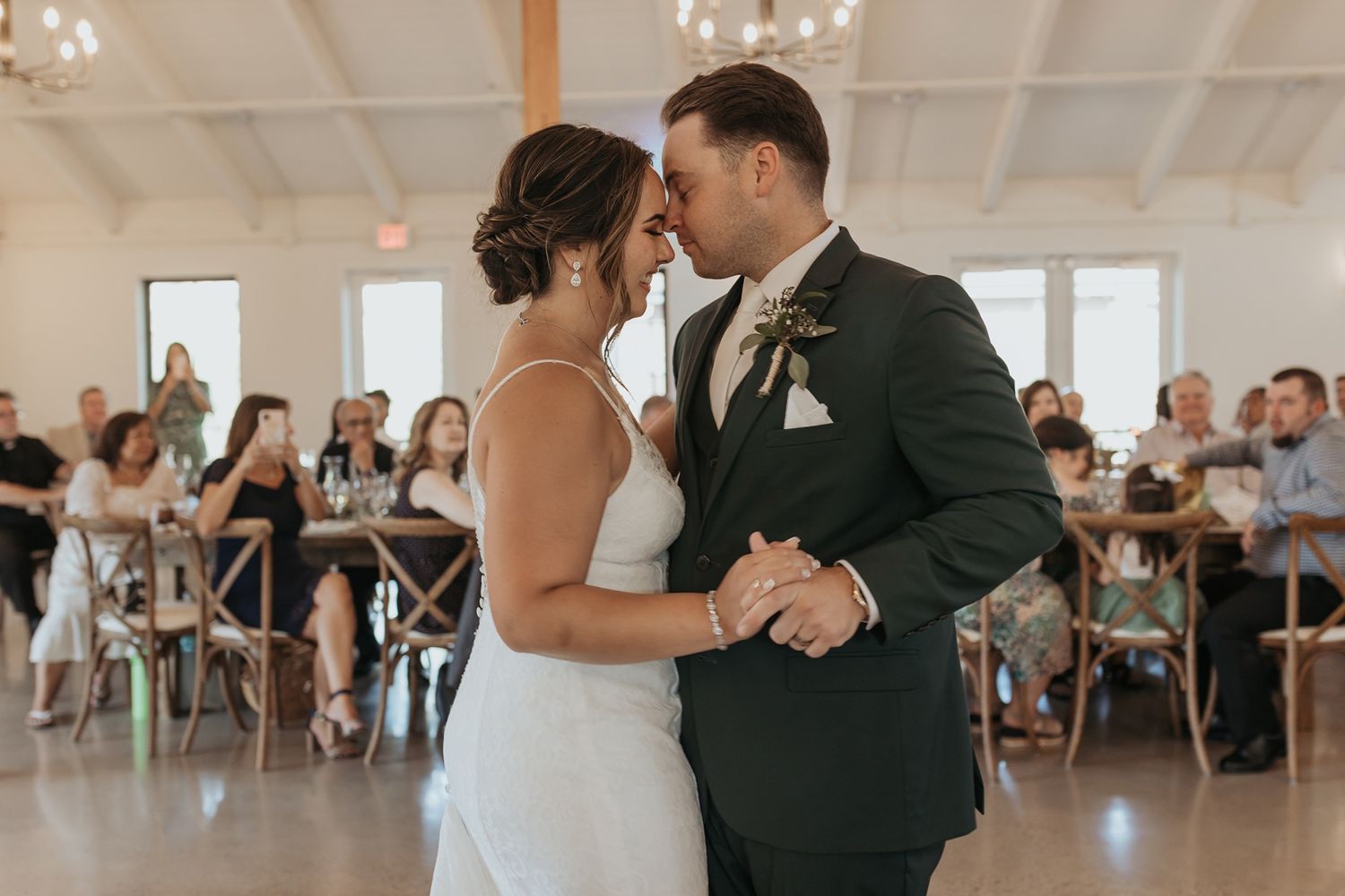 A couple shares their first dance at a wedding reception in a bright white venue with guests watching from their tables at Canopy Grove.