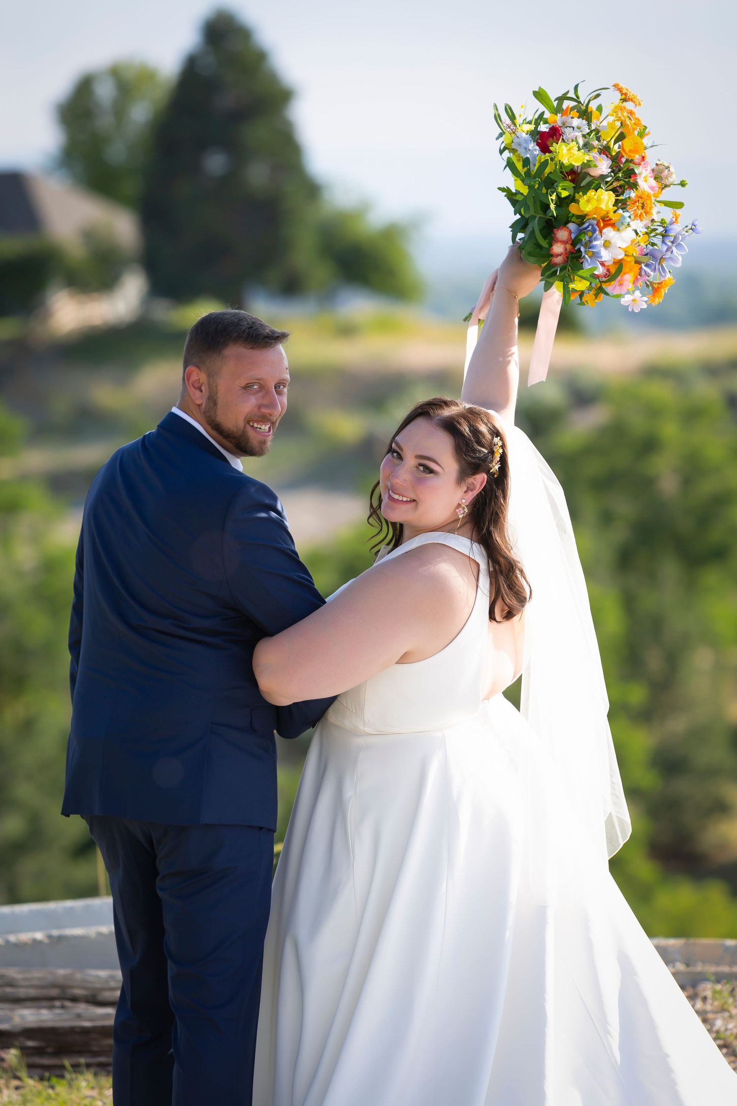 bride and groom looking over their shoulders at camera bride holding bouquet in the air. Boise wedding photographer.