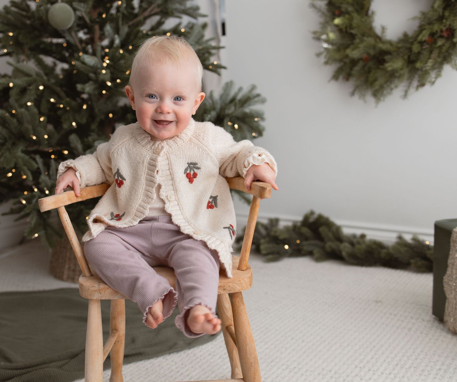 Child sitting in wooden chair near decorated Christmas tree with twinkling lights. Photography in Buckinghamshire.