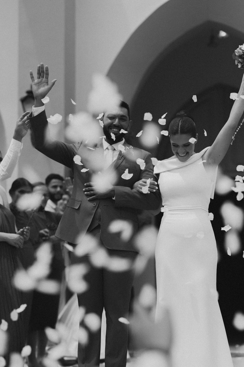 Black and white wedding photo showing couple celebrating as white rose petals fall around them during reception.