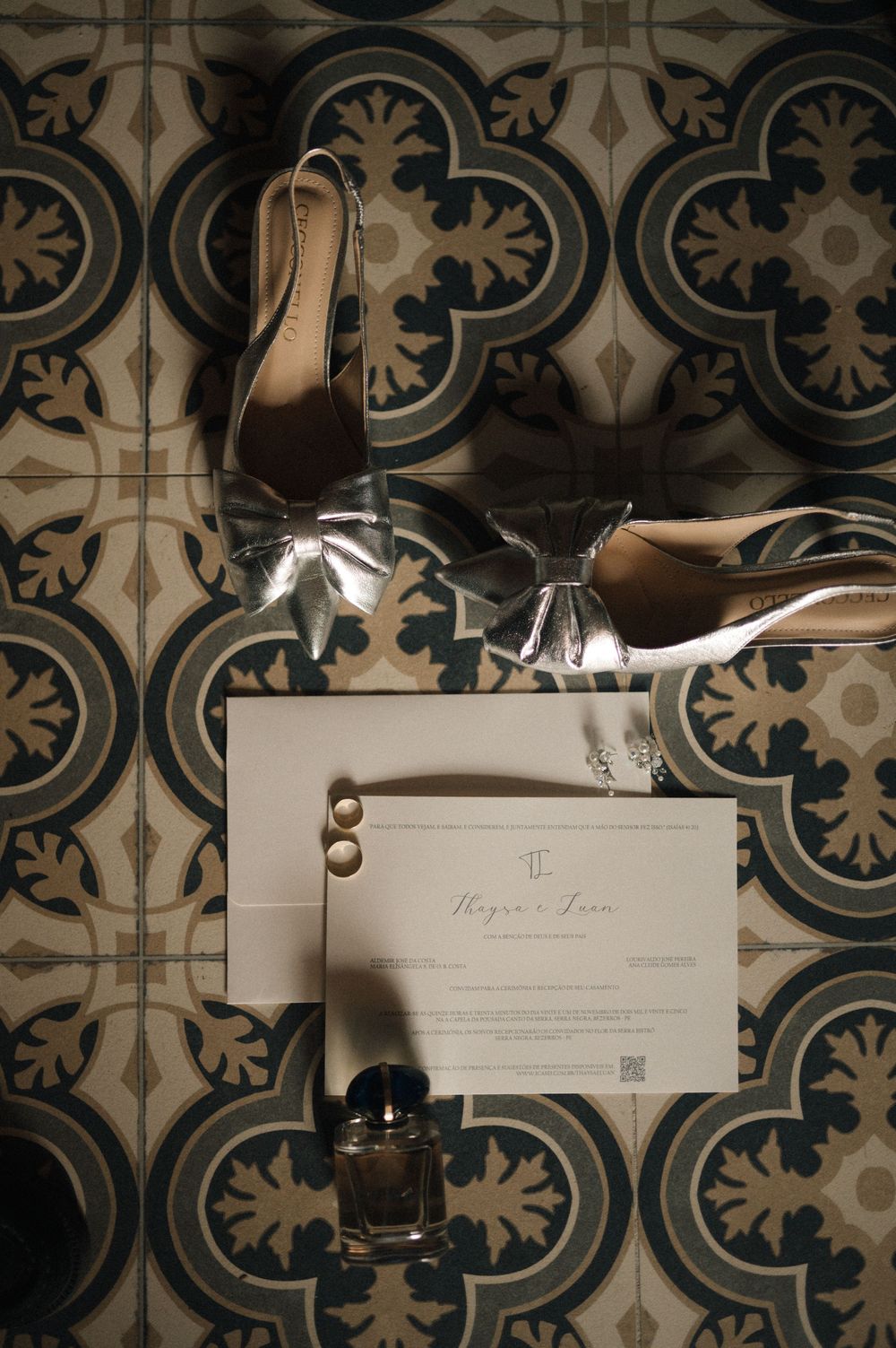 Wedding invitation card with elegant high heels and perfume bottle arranged on ornate patterned tile floor.