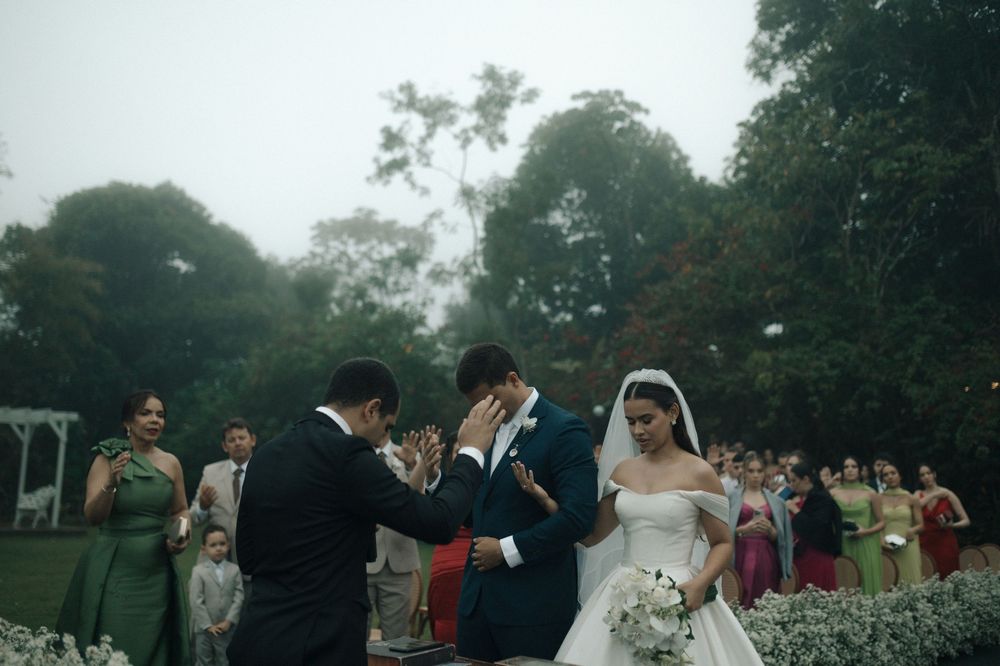 A wedding ceremony takes place outdoors in a garden setting with guests gathered around on a misty afternoon.