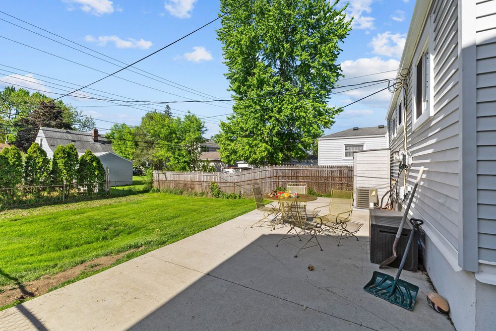 Spacious backyard with concrete patio, outdoor furniture, and lush green lawn beside a gray house.