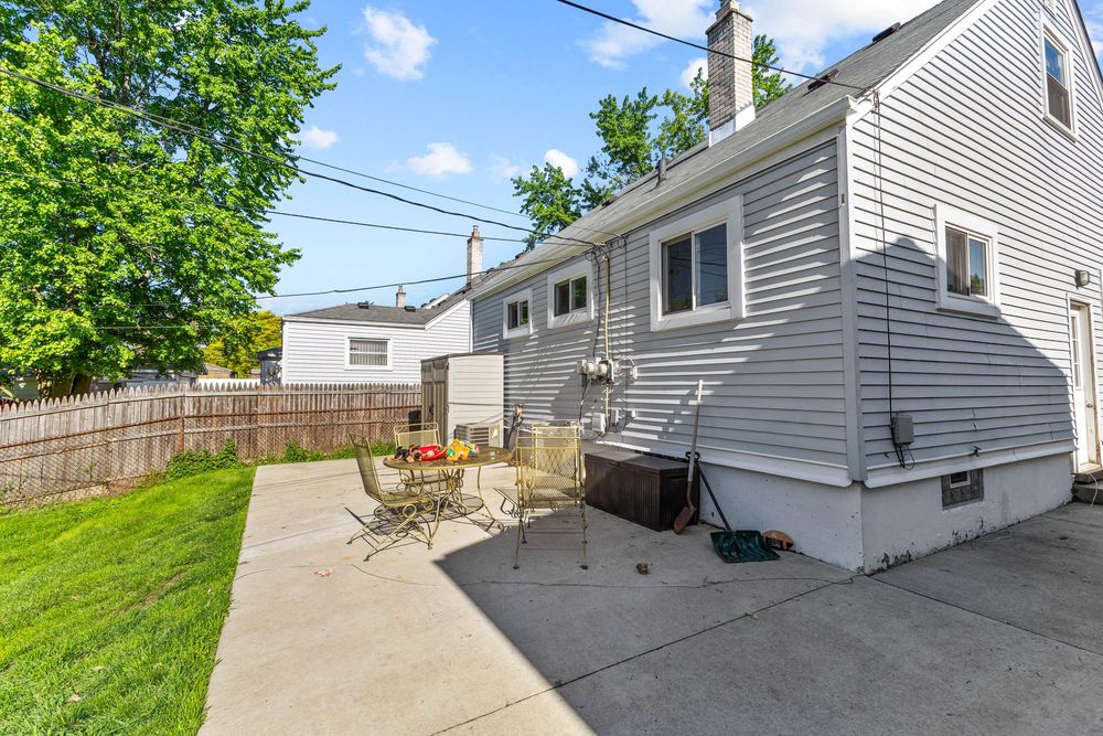 Backyard patio with outdoor dining set and hot tub beside a gray sided home with wood fence.
