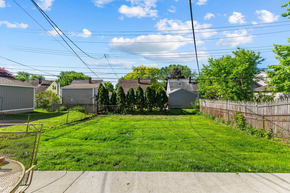 Large fenced backyard with green lawn, mature trees, and storage sheds on a sunny day.