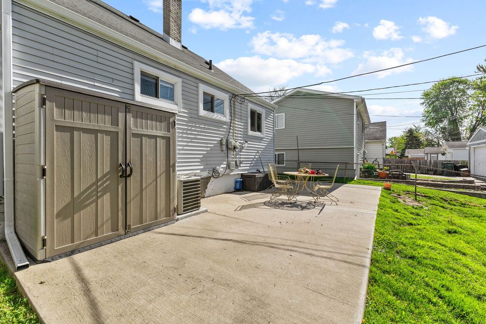 Backyard patio featuring a wooden storage shed, concrete pad, green grass, and outdoor fire pit.