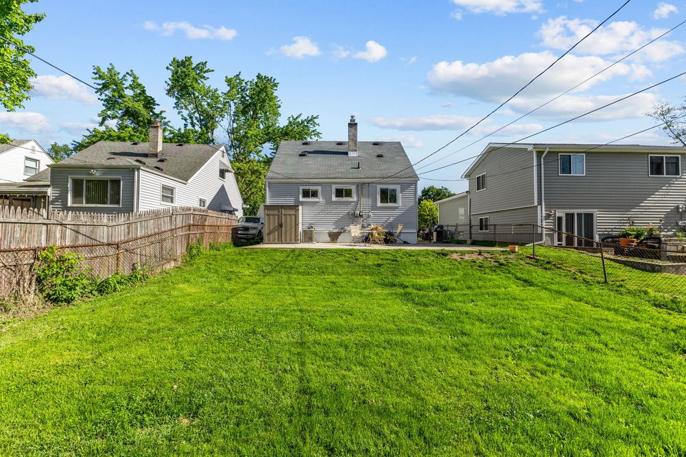 Expansive green backyard lawn with mature trees, wood fence, and rear view of a two-story home.