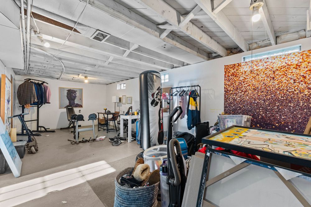 Unfinished basement used as a home gym and art studio with exposed ceiling and concrete floors.