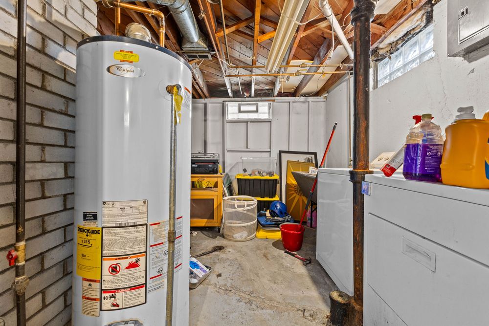 Unfinished basement utility area with water heater, washer, dryer, and brick foundation walls.