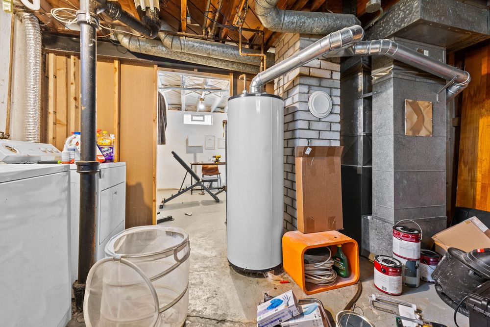 Basement utility room featuring a water heater, furnace, exposed pipes, and brick chimney column.