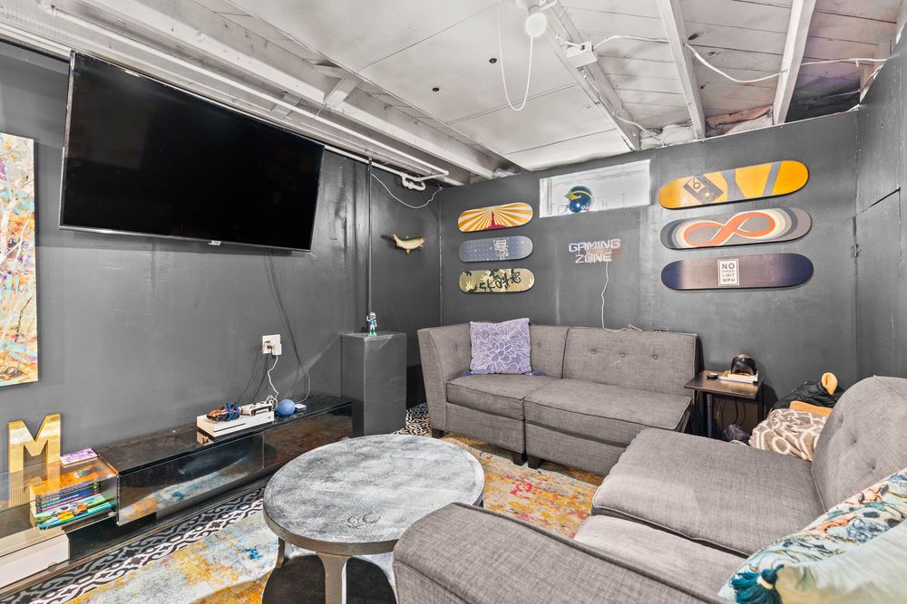 Basement entertainment room with gray walls, mounted TV, sofa, and decorative skateboard wall display.