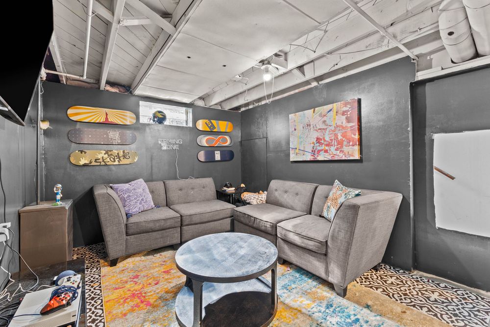 Modern lounge with gray sectional sofas, skateboard wall decor, colorful artwork, and a round coffee table on a vibrant rug.