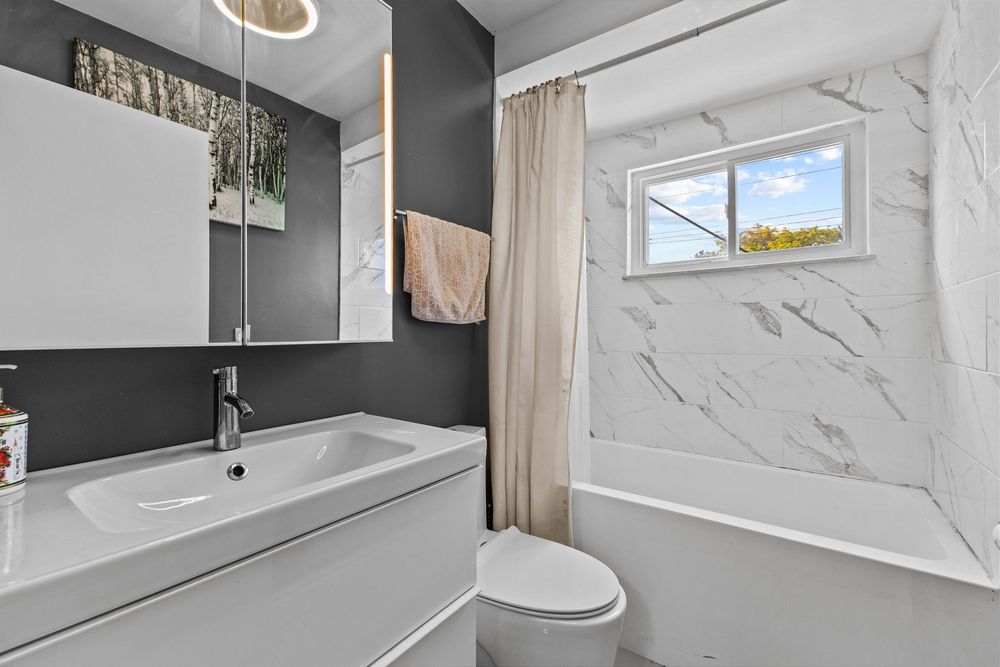 Contemporary bathroom with white floating vanity, marble-style tiled tub surround, and a frosted window above the bathtub.