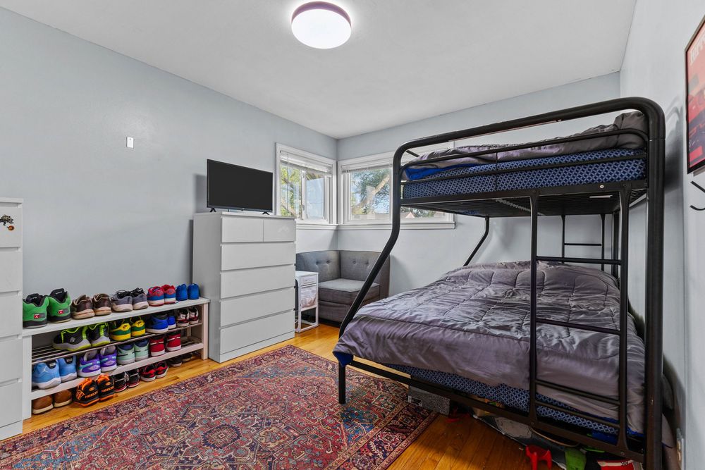 Kids bedroom with black metal bunk bed, shoe rack, dresser, and hardwood floors topped with a colorful area rug.