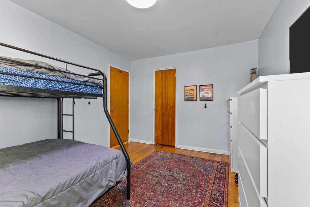 Simple bedroom featuring a black metal bunk bed, wooden dresser, and hardwood floors with a patterned area rug.