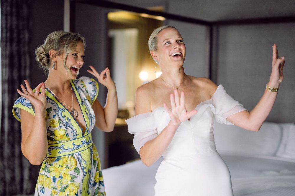 People laughing and dancing together at a celebration wearing yellow floral and white dresses.
