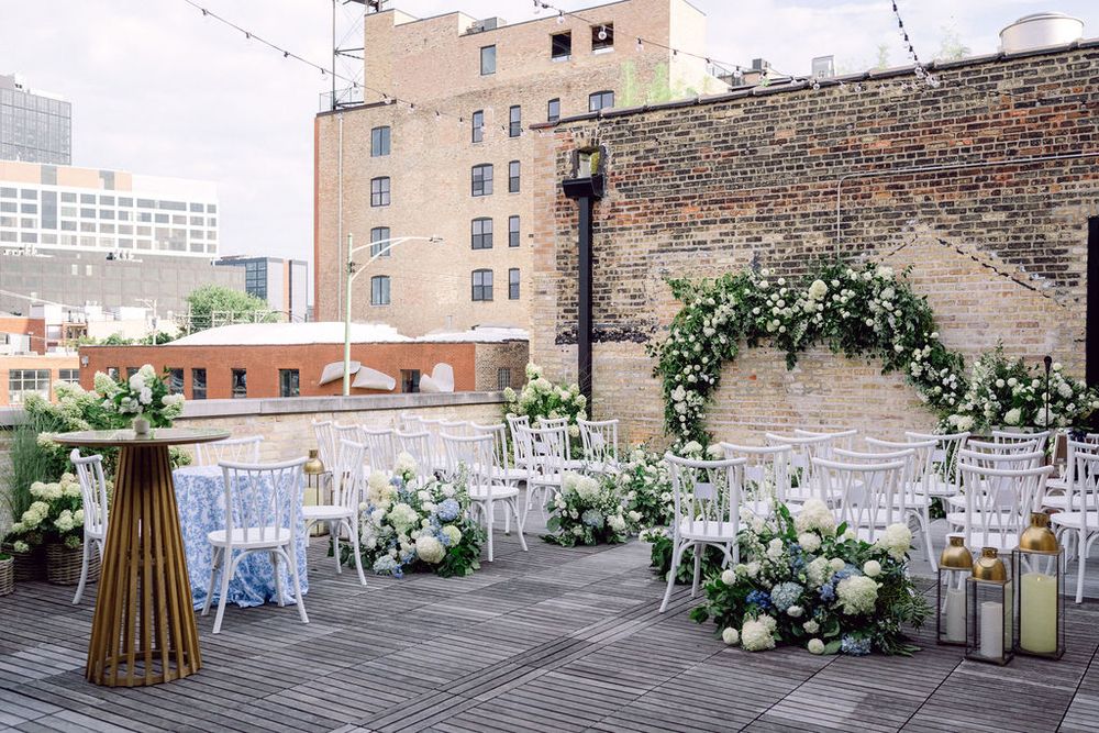 An outdoor wedding venue setup with white chairs and floral arrangements against an urban brick building backdrop.