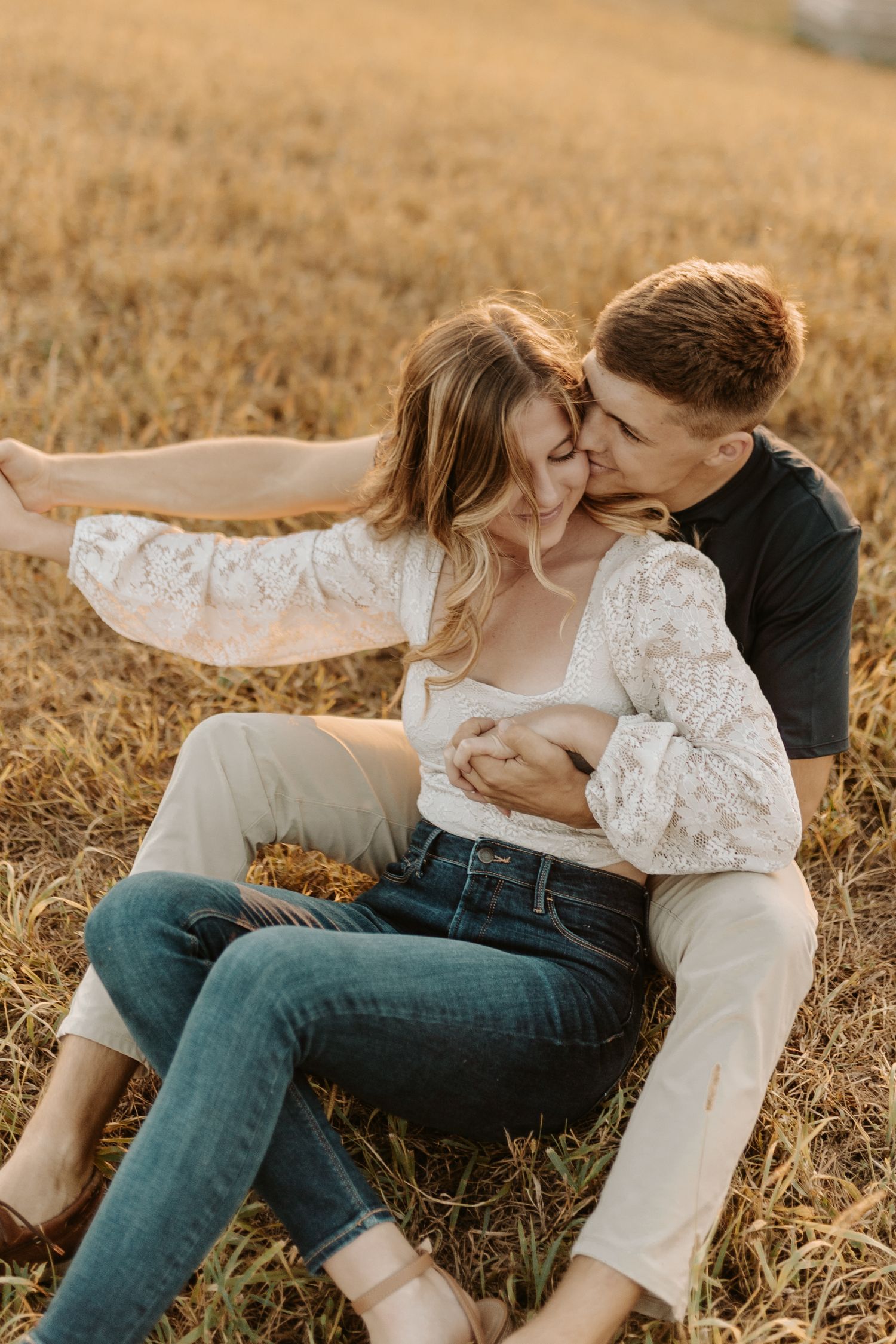 A romantic couple embrace in a golden wheat field at sunset.