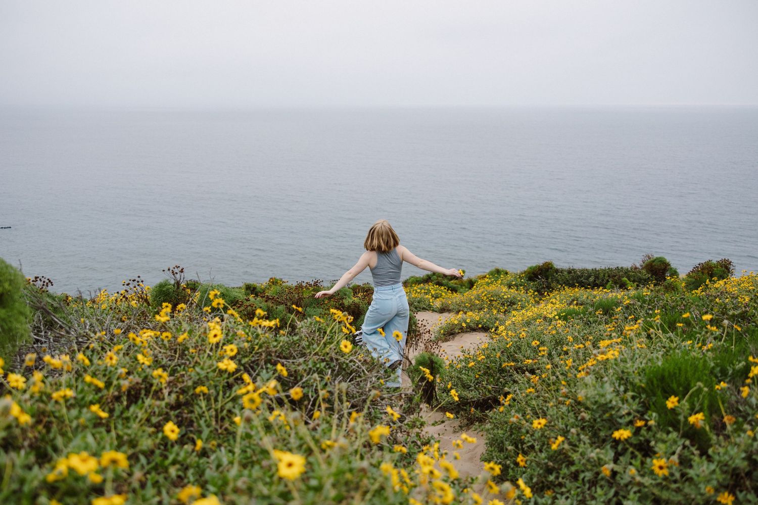 Senior portrait session of a girl dancing in yellow flowers overlooking the ocean