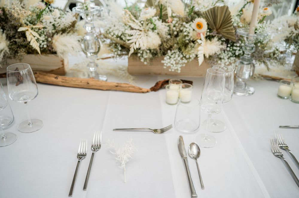 Elegant wedding reception table settings with white floral centerpieces and crystal glassware on white tablecloths.