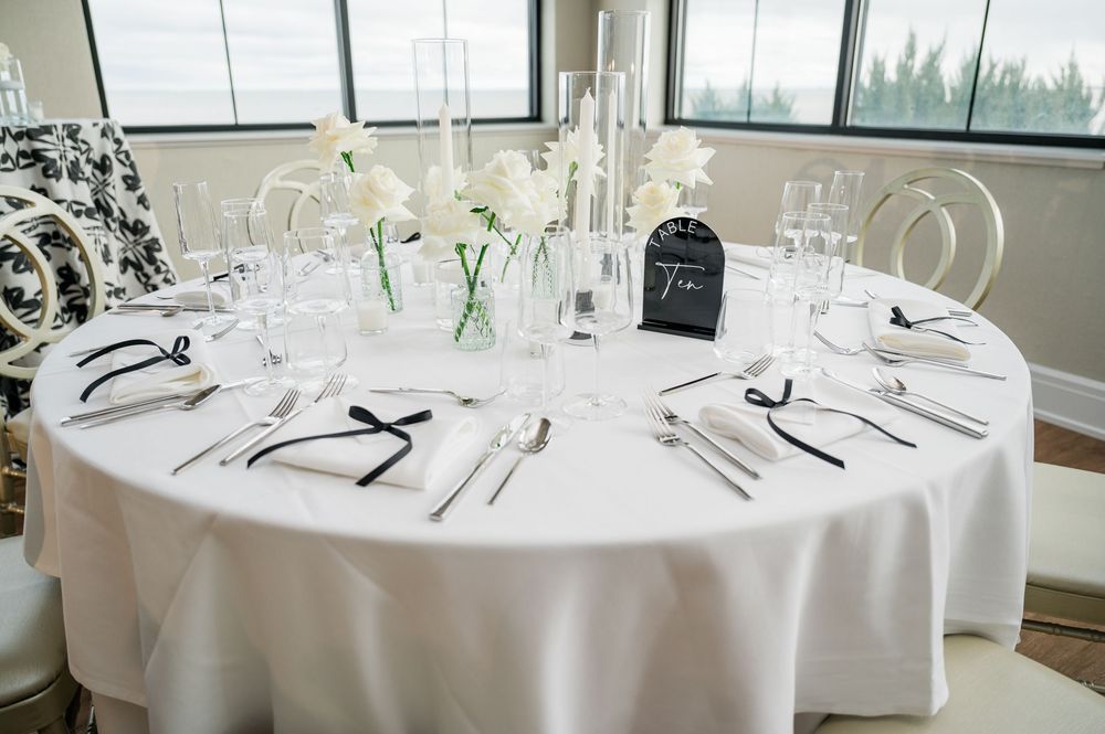 Elegant white round dining tables set with crystal glassware and formal place settings in a bright restaurant space.