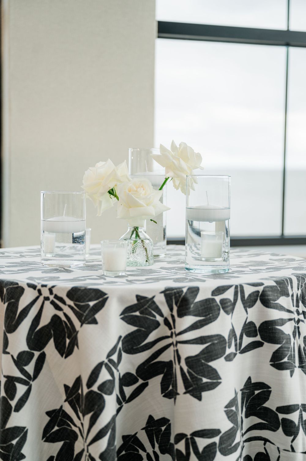 Elegant black and white floral tablecloths with white flower centerpieces in a banquet setting.