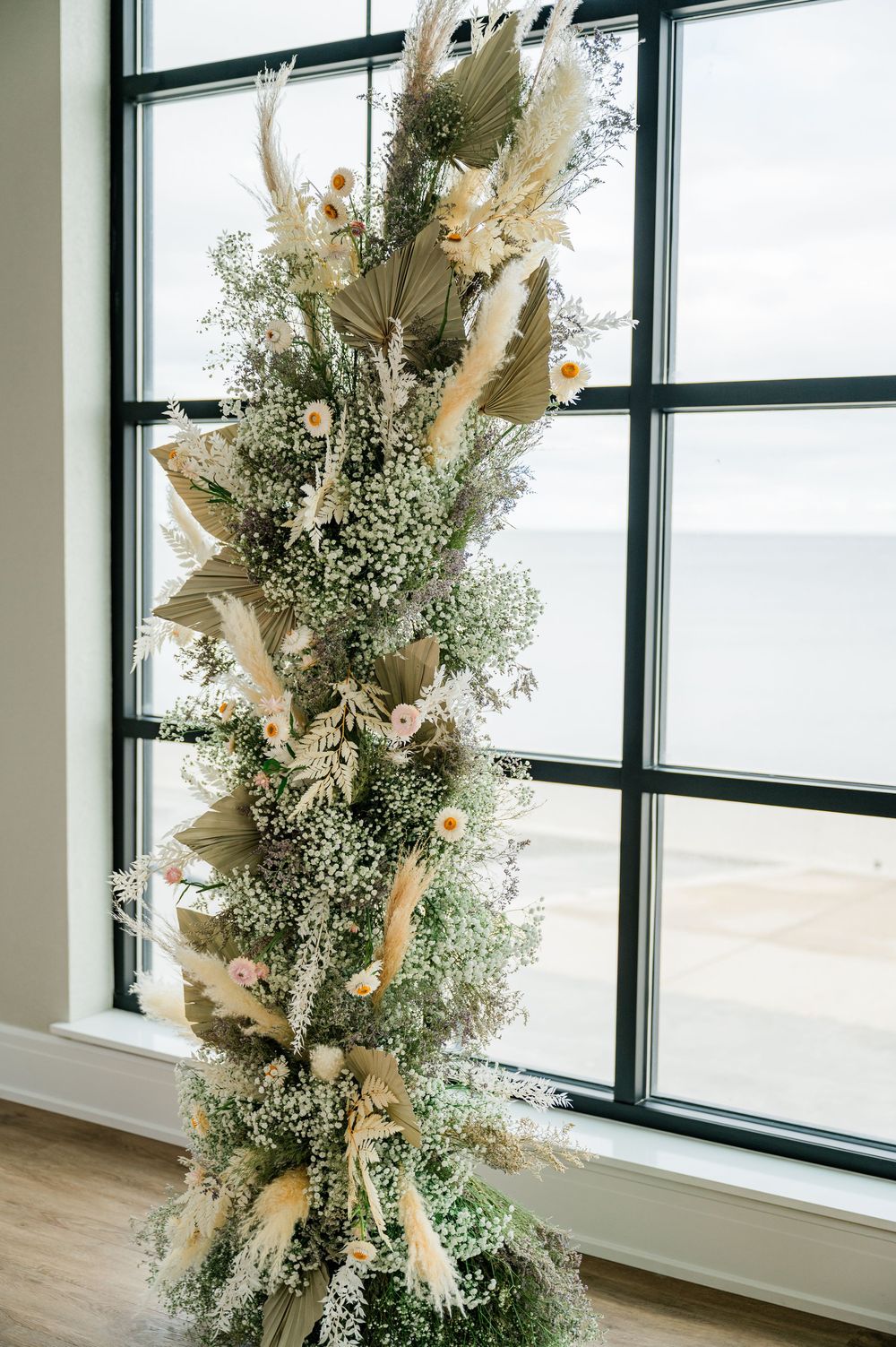 Elegant dried pampas grass and baby's breath floral arrangement displayed against a window in a modern venue.