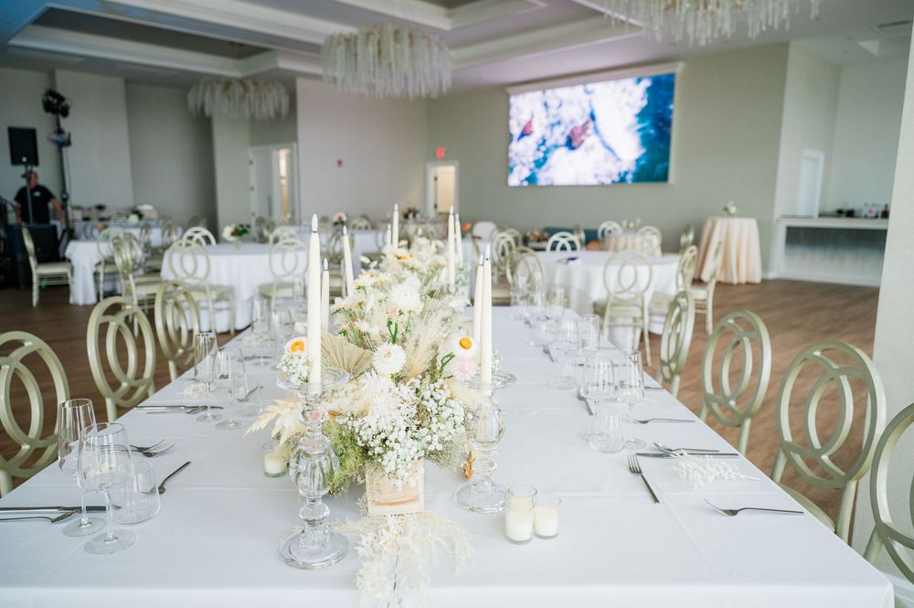 Modern wedding reception venue with white tables and gold chairs under crystal chandeliers.