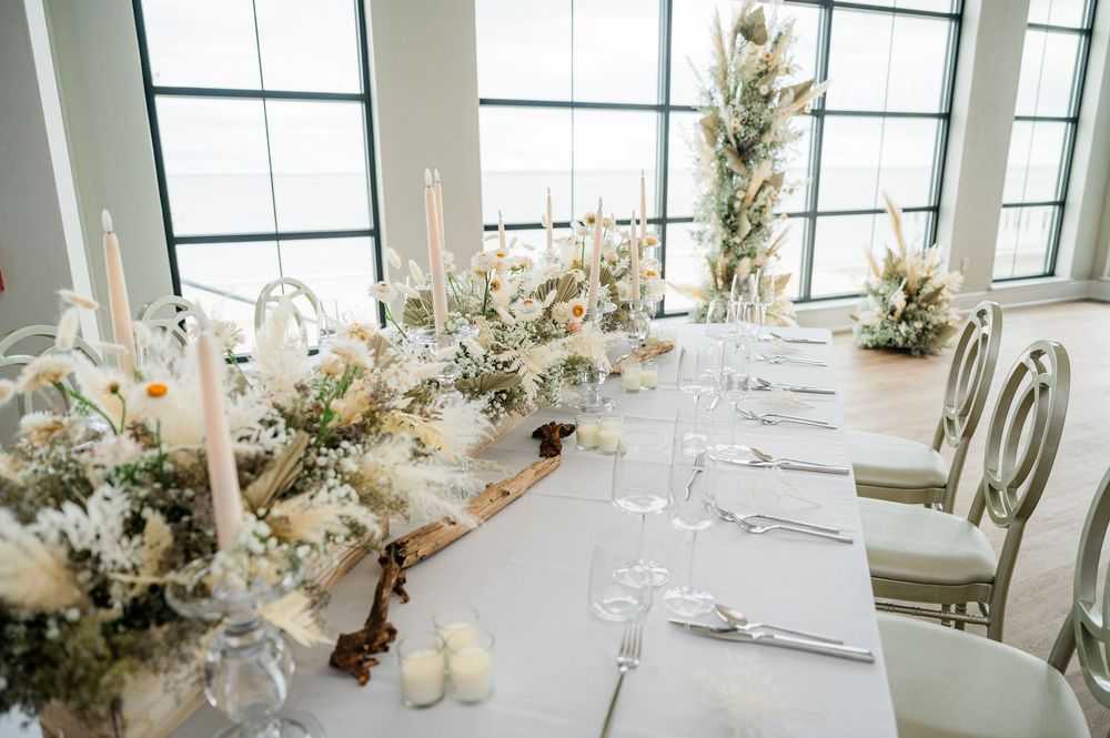 Elegant white floral centerpieces with orchids and candles on dining tables in bright room.