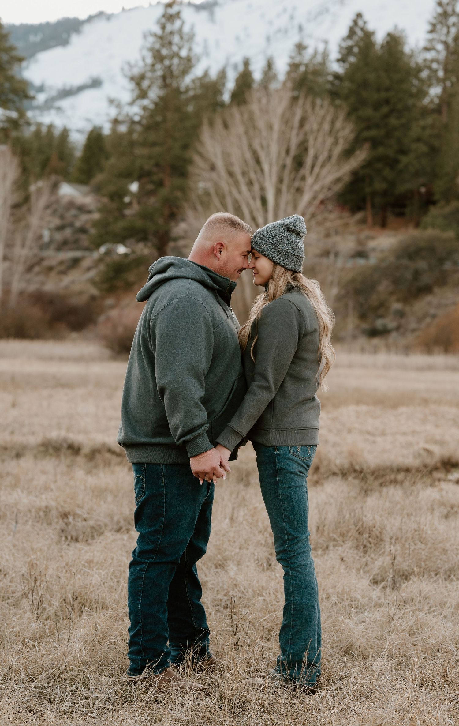 Two people in matching green sweaters share an intimate moment together in a rustic outdoor field setting.