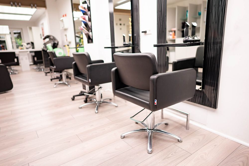 Modern hair salon interior with sleek black styling chairs, white walls, and minimalist decor in a bright open space.